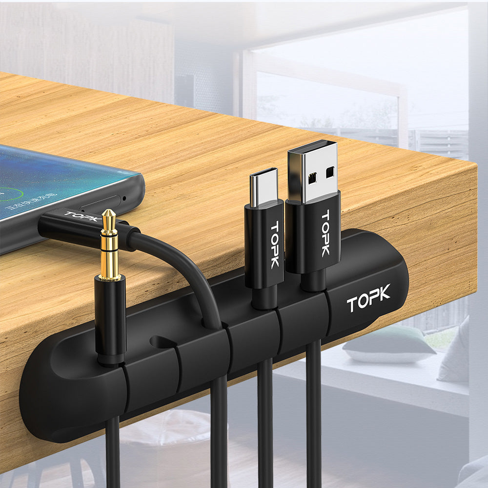 Giggly Gear black desk cable organiser attached to wooden desk holding multiple charging and audio cables